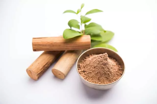 Une photo qui illustre trois morceaux de bois de santal et de la poudre de santal. Des feuilles vertes sont posées en haut des morceaux de bois.