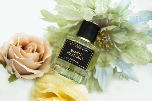 Una foto que ilustra el perfume Vanilla Alcantara colocado entre tres flores. La primera flor de la izquierda es beige, la segunda flor de abajo es amarilla, la tercera flor de arriba es verde.