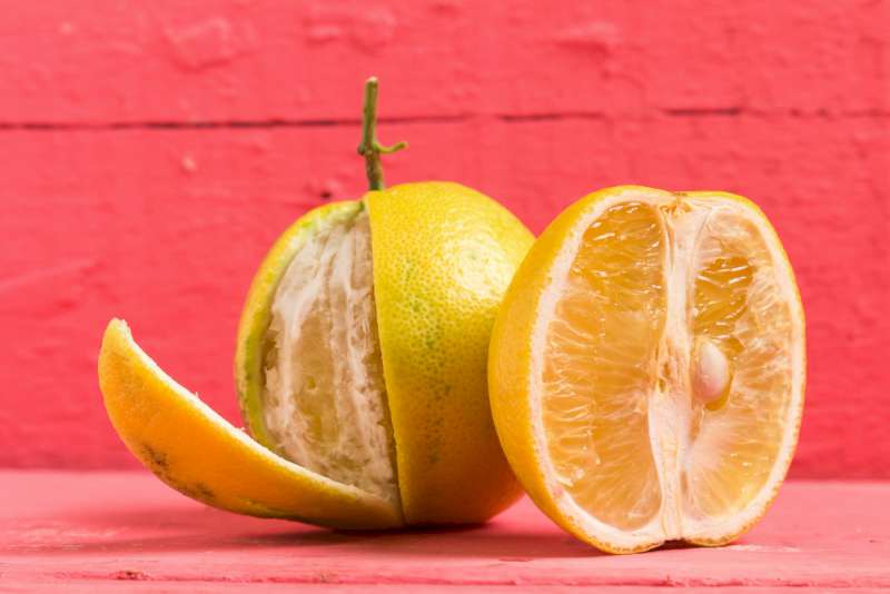 Une photo illustrative de deux fruits de bergamote. La première est coupée à demi et la deuxième est derrière et complète. Une partie de sa peau est enlevée à moitié.