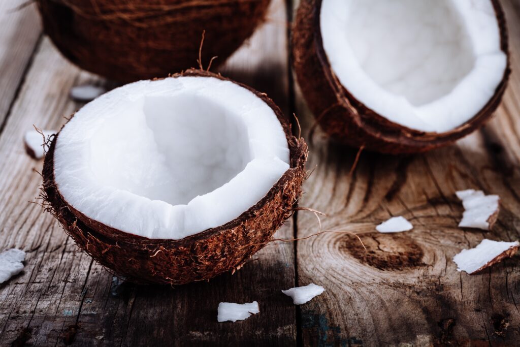 Une photo de la noix de coco coupée en deux, posée sur une table en bois pour délivrer ses odeurs tropicales tant aimées en parfumerie.