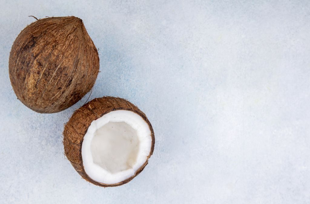 Les parfums noix de coco sont fruités et très exotiques - Une photo de deux noix de coco posées sur un sol blanc, la première est complète, la deuxième est à demi.